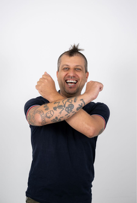 Mann mit Piercings und Tattoos kreuzt lachend die Arme vor der Brust, wobei seine Unterarmtattoos gut sichtbar sind.